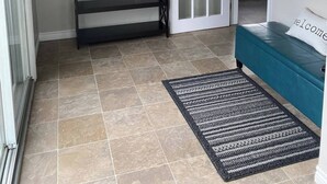 Un couloir avec une console sombre, une plante en pot, un tapis à motifs, un banc de couleur turquoise et une porte donnant sur la cuisine.