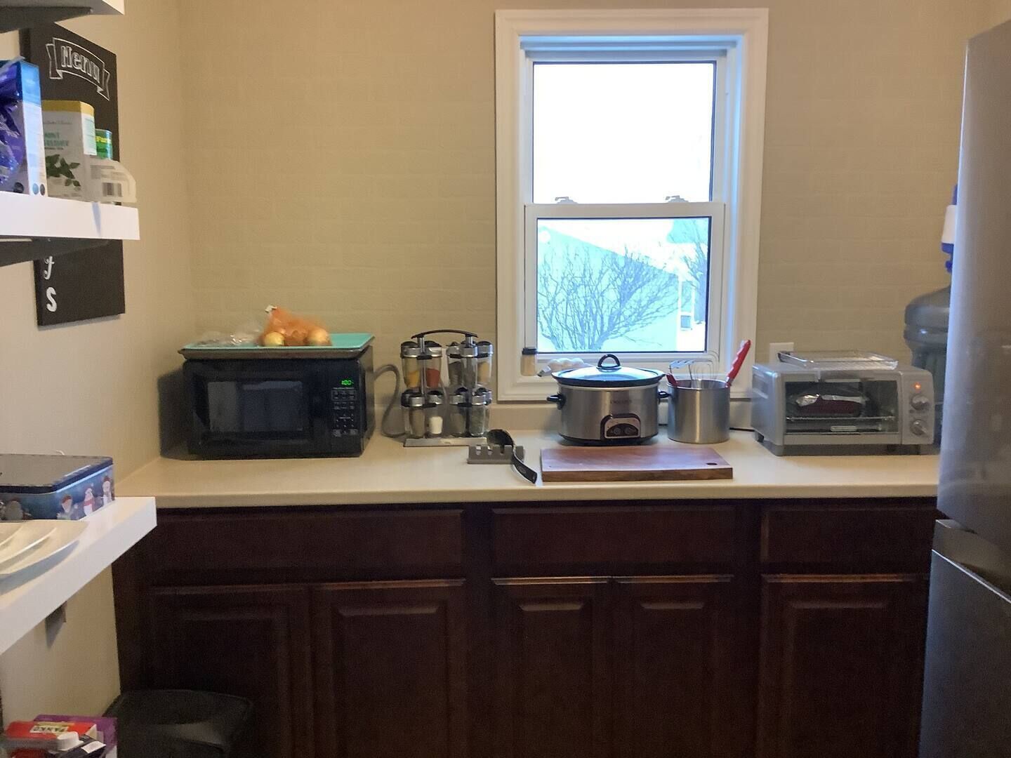 A kitchen with a microwave, slow cooker, toaster, and a window with a view of trees.