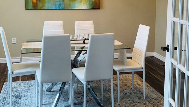Un coin repas avec une table ronde, quatre chaises, un lustre et un grand tableau abstrait accroché au mur.