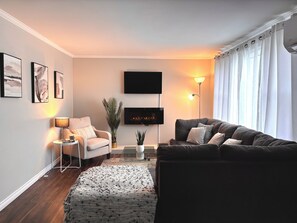 A modern living room with a sofa, armchair, and a flat-screen TV mounted on the wall. - Quite 5 room home near the ocean in town (Stephenville)