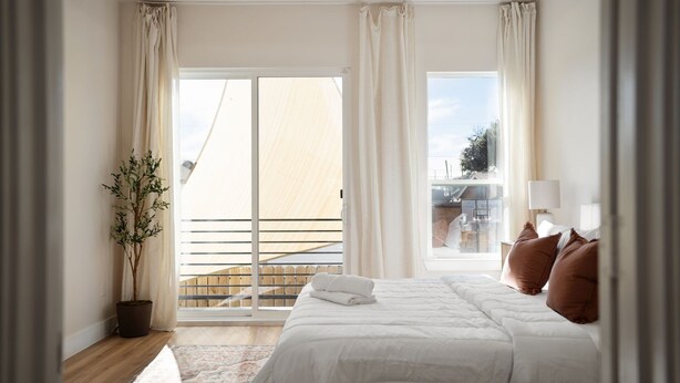A bedroom with a large bed, a potted plant, a view of a balcony, and a window with curtains. - Cozy/Modern King Suite in Houston Texas (Houston)