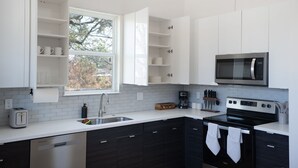 A modern kitchen with white cabinets, a stainless steel microwave, a black stove, and a window with a view of trees. - Cozy/Modern King Suite in Houston Texas (Houston)