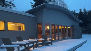 A modern building with a covered outdoor seating area and a snow-covered deck. - Contemporary Berkshire Home with Views of Taconic Golf Course (Williamstown)