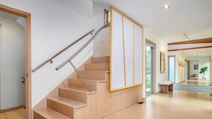 A modern staircase with wooden steps and metal handrails, leading to a hallway with a view of the outdoors. - Contemporary Berkshire Home with Views of Taconic Golf Course (Williamstown)