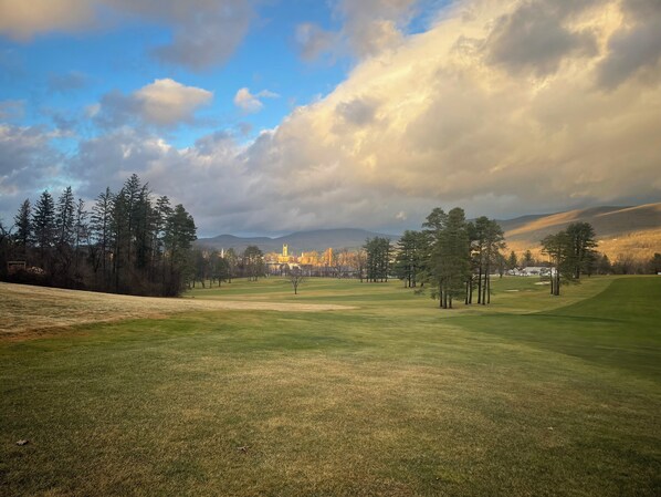 Ein Golfplatz mit blauem Himmel, Bäumen und Gebäuden in der Ferne.