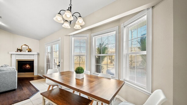 A dining area with a wooden table, white chairs, and a fireplace. - Hot Tub/Gameroom/Firepit/ Coler MTB - Downtown (Bentonville)