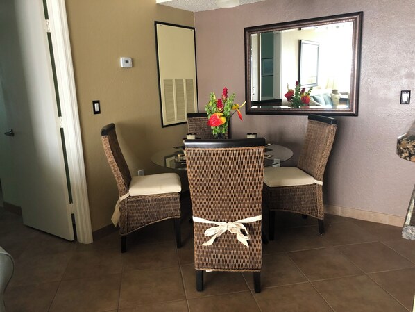 A dining area with wicker chairs and a round table, a mirror on the wall, and a door leading to another room.