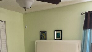 Een bed met een wit hoofdeinde, een matras en opgevouwen handdoeken. Boven het bed hangen twee ingekaderde foto's aan de muur.