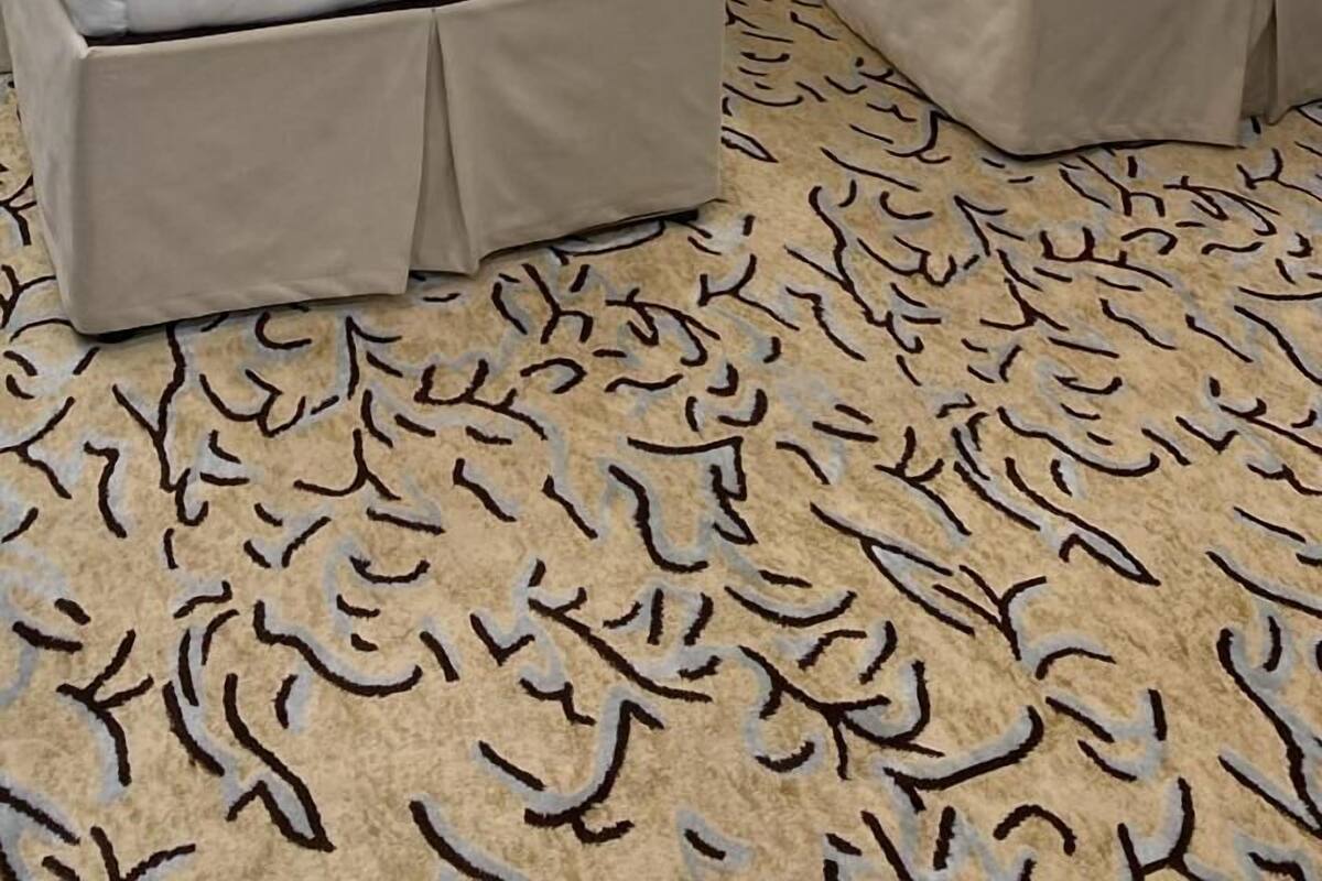A hotel room with two beds, a nightstand with a lamp, and a patterned carpet.