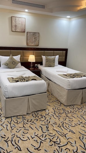 A hotel room with two beds, a nightstand with a lamp, and a patterned carpet. - Masaken Almuna (Jeddah)