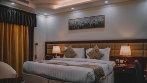 Una camera d'albergo con un letto grande, due comodini con lampade, una testiera e un quadro appeso al muro, oltre a una finestra con tende.