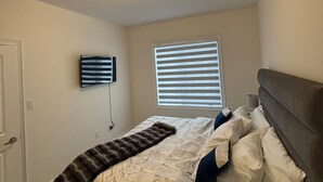 A bedroom with a bed, a TV mounted on the wall, and a window with blinds. - Dreamland by Wonderland (Vaughan)