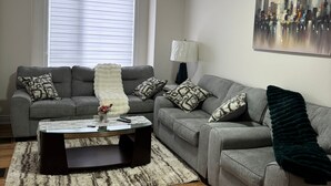 A living room with two grey sofas, a glass coffee table, a white fluffy throw, a cityscape painting, and a window with blinds. - Dreamland by Wonderland (Vaughan)