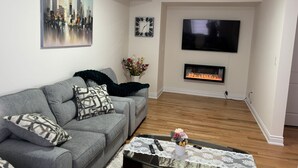 A living room with a grey sofa, a flat-screen TV, a fireplace, and a cityscape painting. - Dreamland by Wonderland (Vaughan)