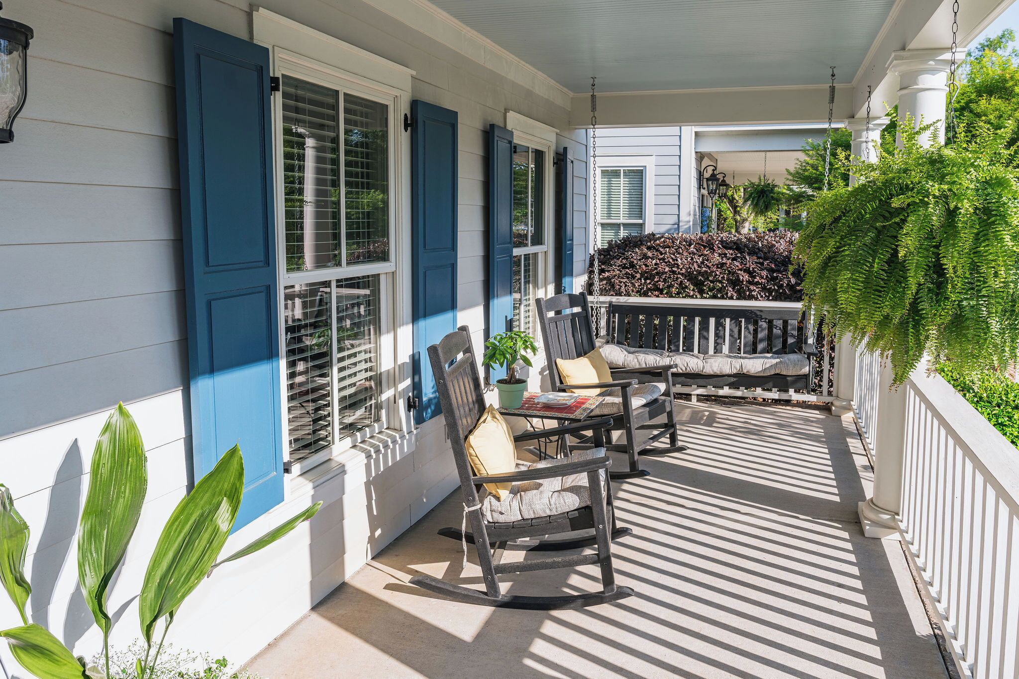A covered porch with rocking chairs and a small table, white siding, and blue shutters.