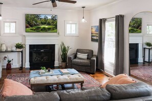 A living room with a fireplace, a television mounted above it, a large mirror, and a seating area with a sofa and ottoman. - 4BR Near Riverview Park Sleeps 8 Masters Ready (North Augusta)