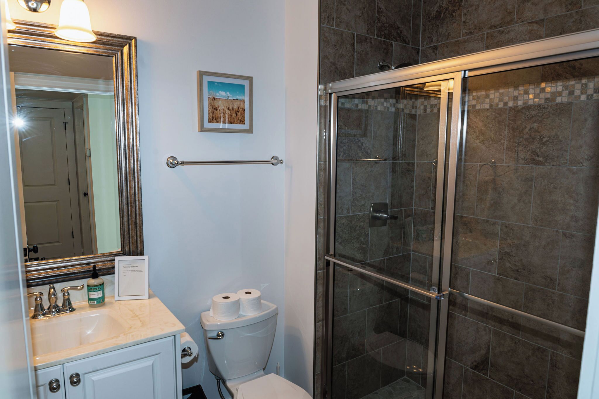 A bathroom with a marble sink, a toilet, a framed picture on the wall, and a glass-enclosed shower.