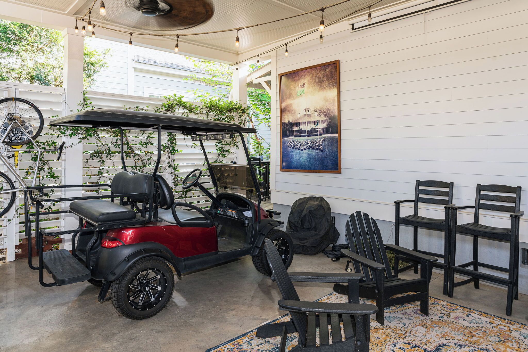 A covered area with a golf cart, chairs, and a painting on the wall.