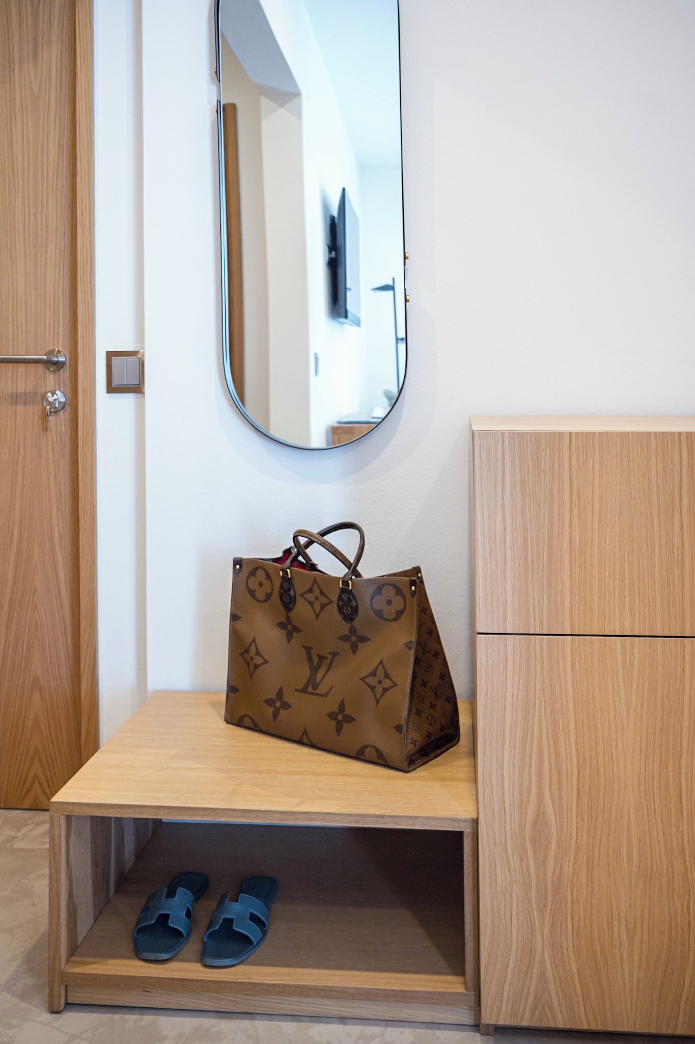 Une coiffeuse en bois, sur laquelle sont posés un sac Louis Vuitton et une paire de pantoufles bleues.