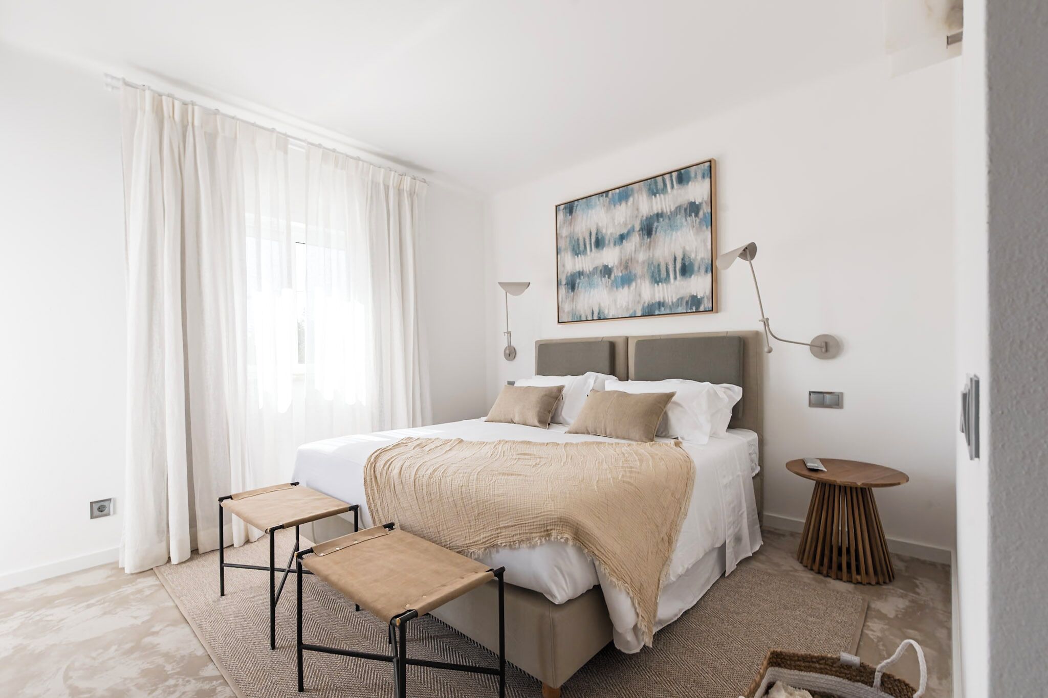 A modern bedroom with a large bed, bedside tables, a bedside lamp, and a painting on the wall.
