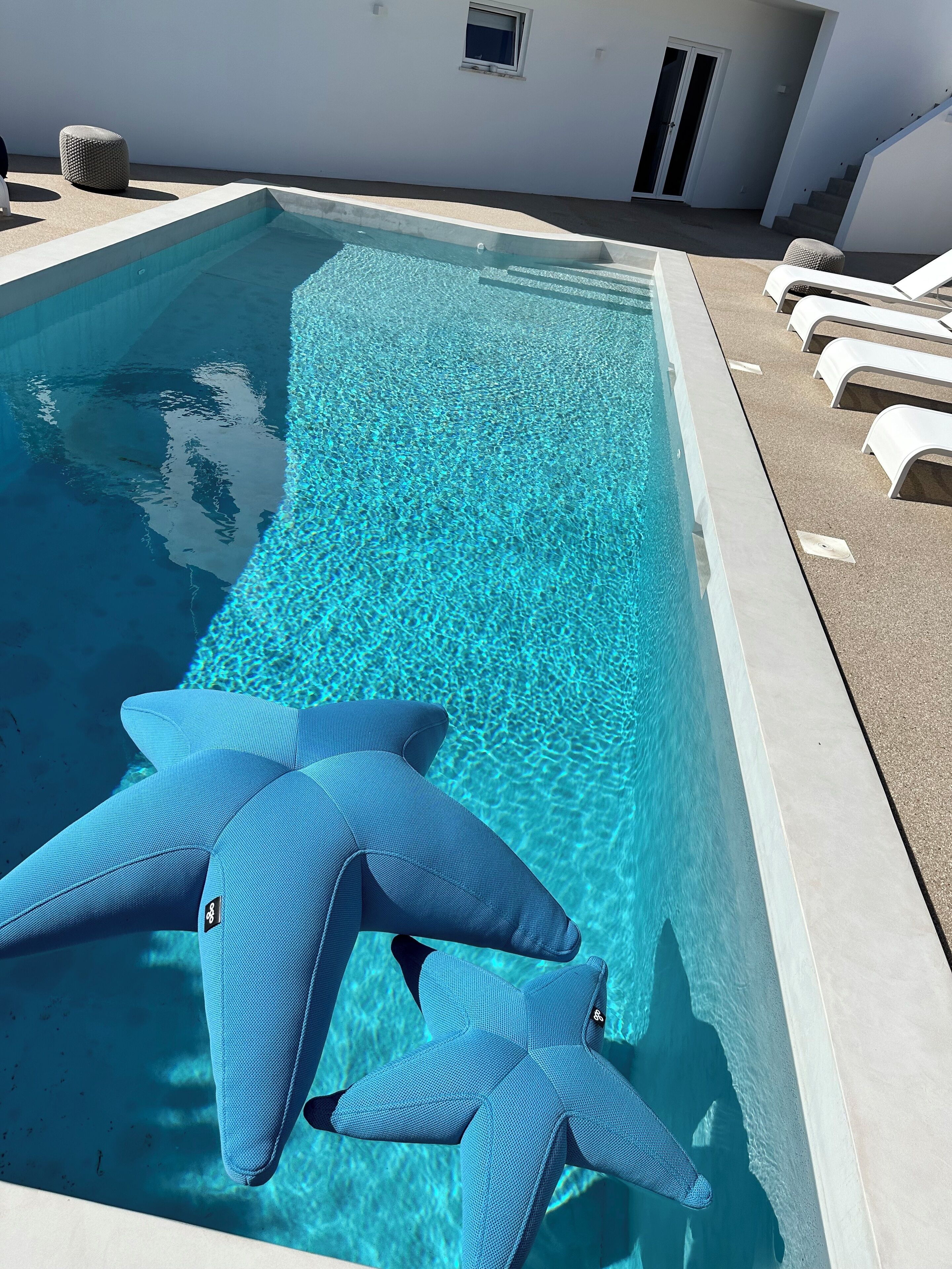 A swimming pool with clear water, surrounded by a white wall and a few lounge chairs.