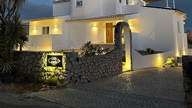 Una villa blanca con entrada de pared de piedra, un pequeño porche y un cartel que indica 'Casa Malta'.