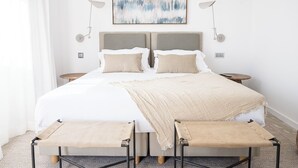 Un dormitorio moderno con una cama grande, dos mesitas de noche, una lámpara de pared y un cuadro abstracto de gran tamaño.