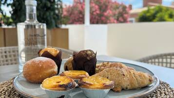 A table with a woven placemat, a plate of pastries including a croissant, a muffin, and a tart, and a bottle of water.