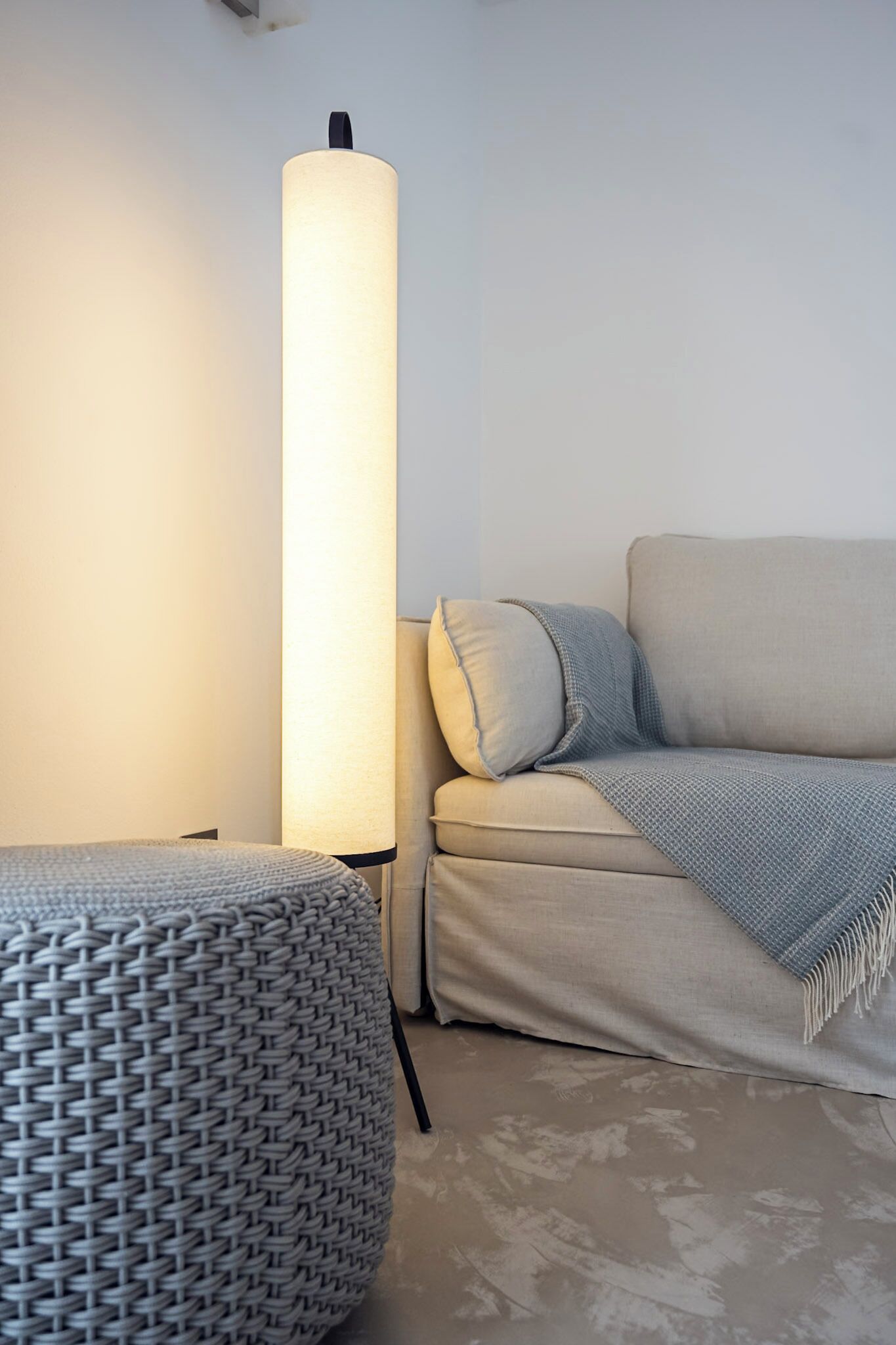 A modern living room with a beige sofa, a round ottoman, and a tall floor lamp.