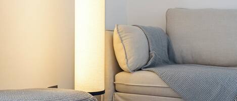 A modern living room with a beige sofa, a round ottoman, and a tall floor lamp.