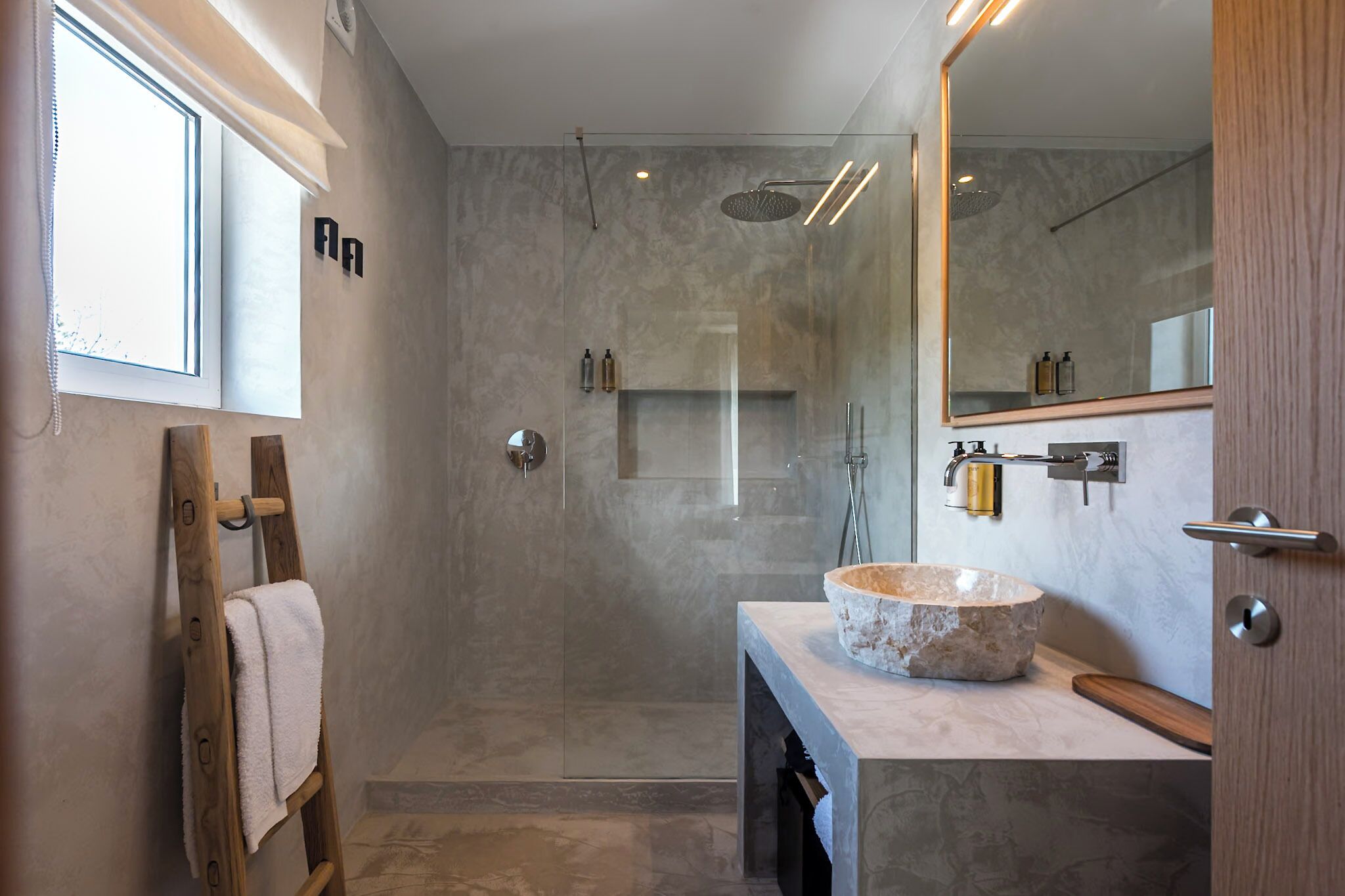 Une salle de bain moderne avec un lavabo en pierre, une douche à parois de verre et une échelle en bois.