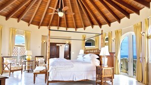 Ein geräumiges Schlafzimmer mit Himmelbett, Holzmöbeln und einem Balkon mit Vorhängen.