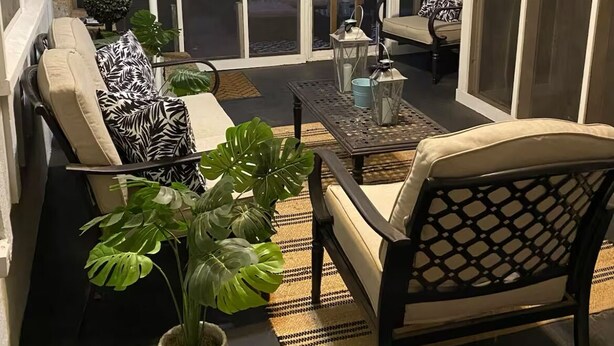 Une véranda aménagée avec un canapé, des fauteuils, une table basse et des plantes en pot.