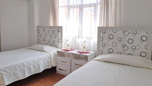 A bedroom with two single beds, a bedside table with a lamp, and a window with sheer curtains. - Apartment in residential area (Sucre)