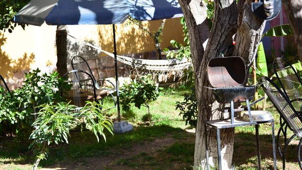 A hammock under a blue umbrella, a metal bird feeder, and a chair in a garden setting. - Apartment in residential area (Sucre)