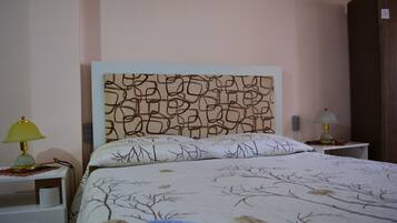 Una cama bien hecha con un cabecero estampado, dos lámparas de noche y una mesita de noche pequeña y blanca con una lámpara.