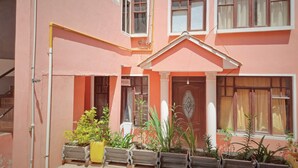 A pink building with multiple windows, a central door with a decorative design, and potted plants in front. - Apartment in residential area (Sucre)