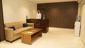 Un área de recepción moderna con un sofá color beige, una mesa de centro de madera y un escritorio de madera oscura con una bandera.