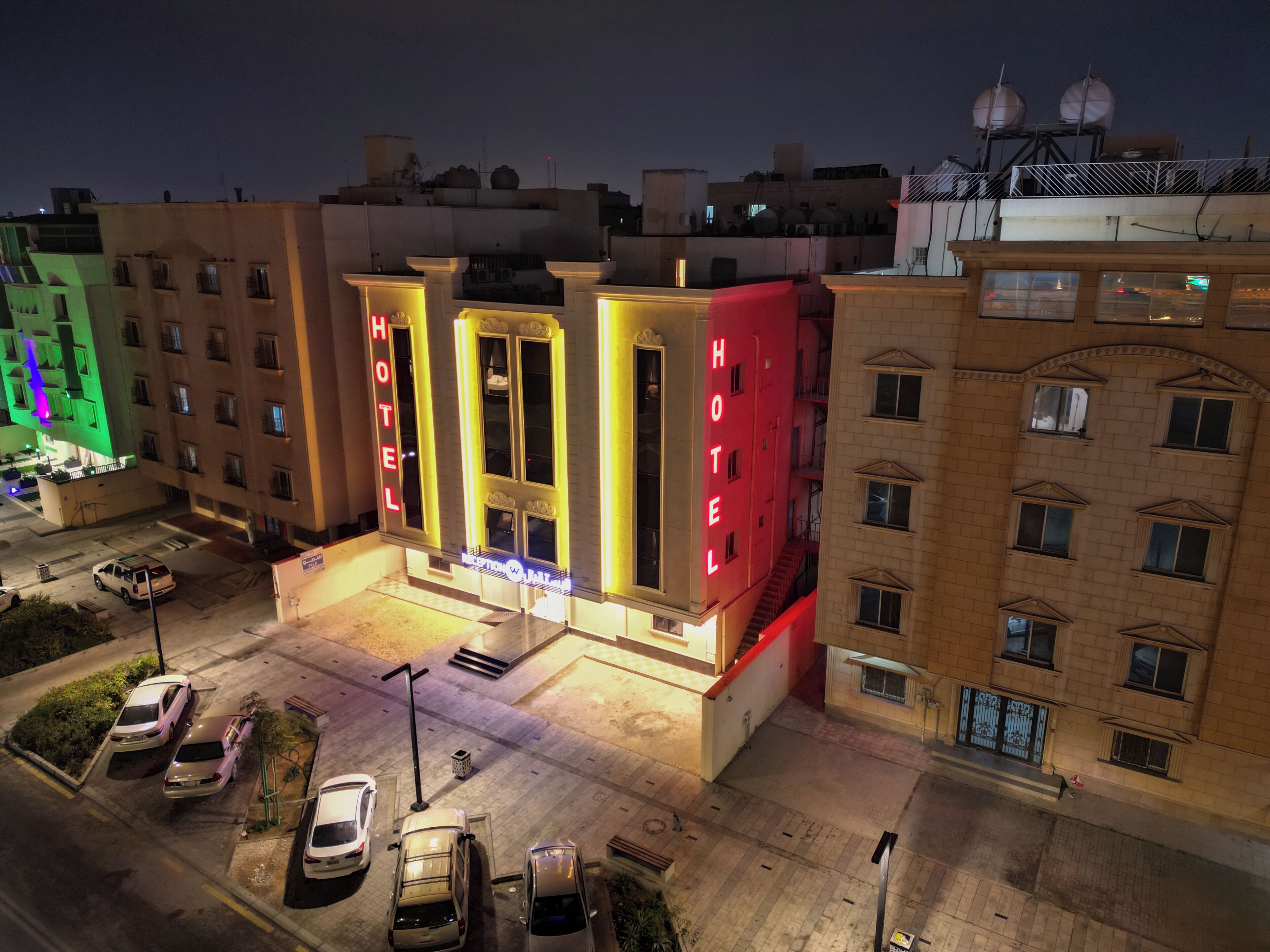 Un hotel con un llamativo letrero de neón, varios pisos y un estacionamiento con varios automóviles.