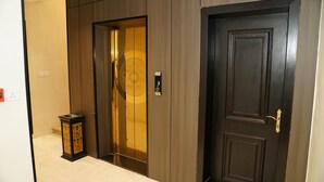 Un ascensor moderno con pantalla digital, una puerta de madera tradicional y un pequeño objeto decorativo en el suelo.