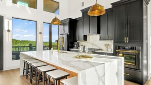 A modern kitchen with a large island, dark cabinetry, stainless steel appliances, and pendant lighting. - Luxury Hilltop, Surreal Views, Pool, Hot Tub, Firepit & 4Kings Bed (Broken Bow)