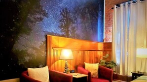 Una habitación acogedora con dos sillones rojos, una mesita con una lámpara y un mural en la pared que representa un cielo estrellado.
