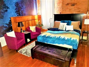 Un dormitorio con cama, mesita de noche, silla, lámpara y vista al cielo nocturno.