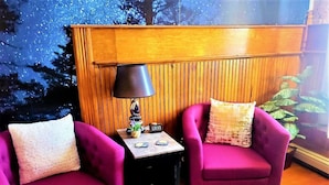 Una habitación con dos sillones morados, una mesita de noche con lámpara y un panel de pared de madera.