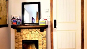 Una chimenea de piedra con un televisor encima, una puerta a la derecha y un cuadro enmarcado a la izquierda.