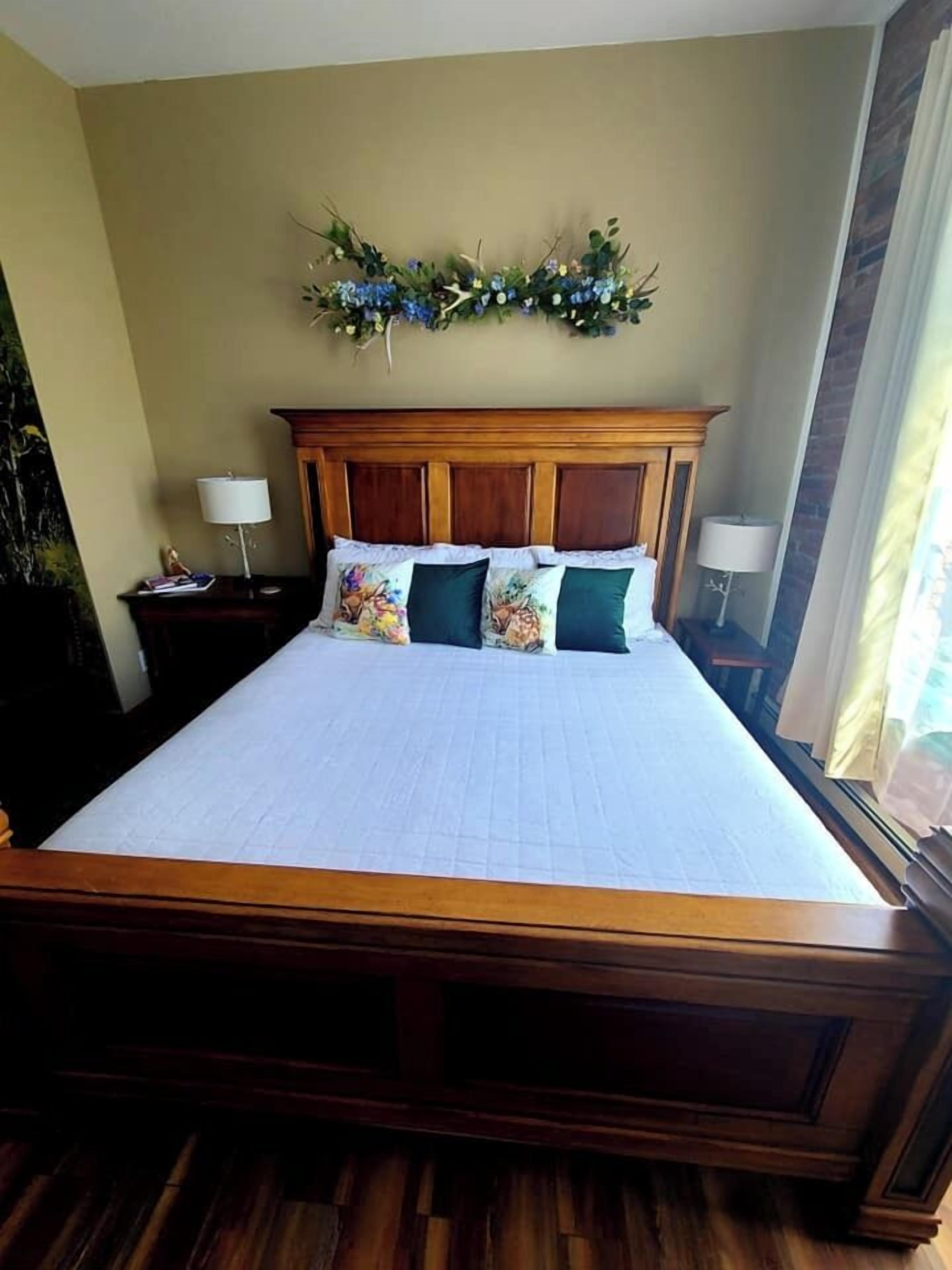 Ein großes Bett mit Holz-Kopfteil, darüber ein Blumengirlande und zwei Nachttischlampen.