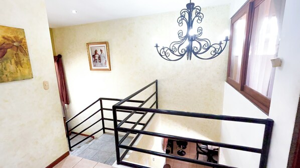 A staircase with a metal railing, a chandelier, a framed picture on the wall, and a window with curtains.