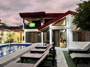 A modern outdoor pool area with lounge chairs and a covered seating area.