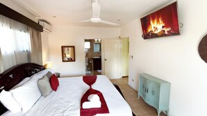 Une chambre d’hôtel avec un lit, un ventilateur de plafond, un tableau représentant un feu, une salle de bain visible à travers une porte ouverte et une armoire bleu clair.
