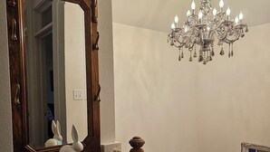A staircase with a wooden handrail and a white picket railing. A large mirror with a wooden frame is mounted on the wall above the staircase. A chandelier hangs from the ceiling.